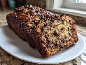 Close-up of moist chocolate chip banana bread, with two slices cut and resting on a white plate.