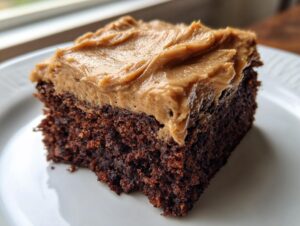 Close-up of a moist slice of dark gingerbread cake topped with thick, creamy caramel-colored frosting.