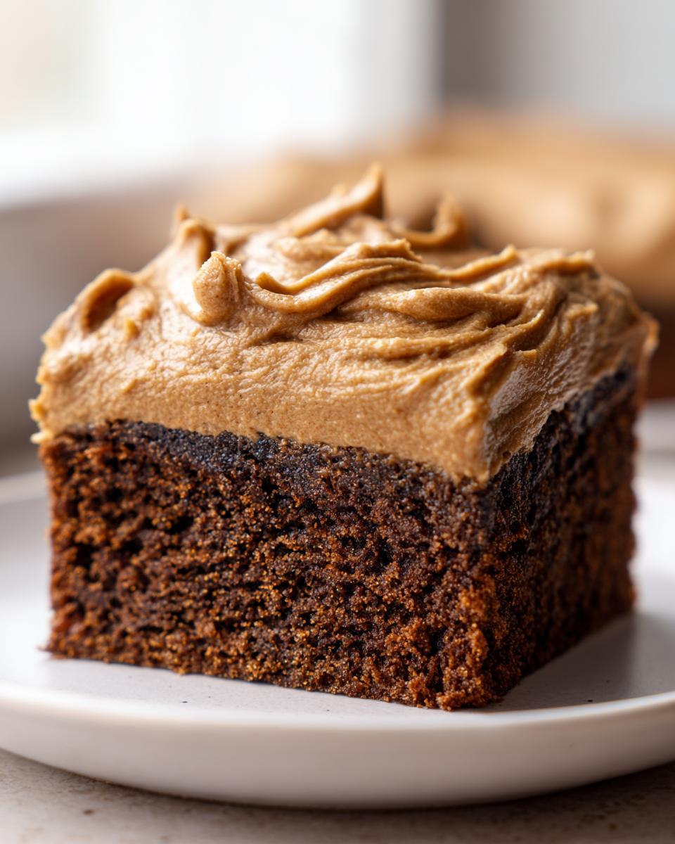 Close-up of a square slice of moist gingerbread cake topped with thick, piped brown frosting.