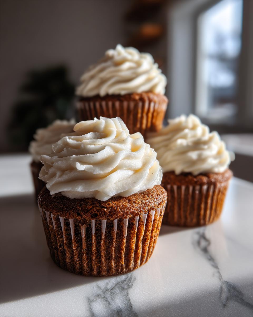 A close-up of several moist gingerbread cupcakes topped with swirls of white cream cheese frosting.