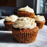 Close-up of four moist gingerbread cupcakes topped with swirls of white cream cheese frosting.