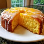 A slice cut from a round orange juice cake topped with a white glaze and orange zest.