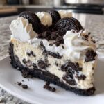 A decadent slice of Oreo cheesecake featuring a dark crust, creamy filling with cookie chunks, topped with whipped cream and whole Oreos.