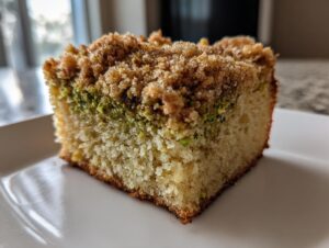 Close-up of a square slice of pistachio coffee cake showing the moist crumb, green pistachio layer, and sugary streusel topping.