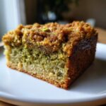 Close-up of a moist slice of pistachio coffee cake showing green crumb and brown streusel topping.