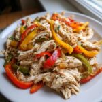 Close-up of shredded chicken mixed with colorful bell pepper strips for crockpot chicken fajitas.