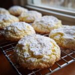 Close-up of soft, crinkle-topped cool whip cookies generously dusted with powdered sugar, cooling on a wire rack.