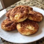 A stack of soft, freshly baked snickerdoodle cookies generously coated in cinnamon sugar, resting on a white plate.