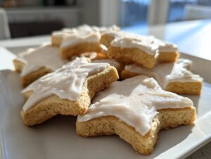 Close-up of star-shaped vegan sugar cookies piled on a white plate, topped with thick white frosting.