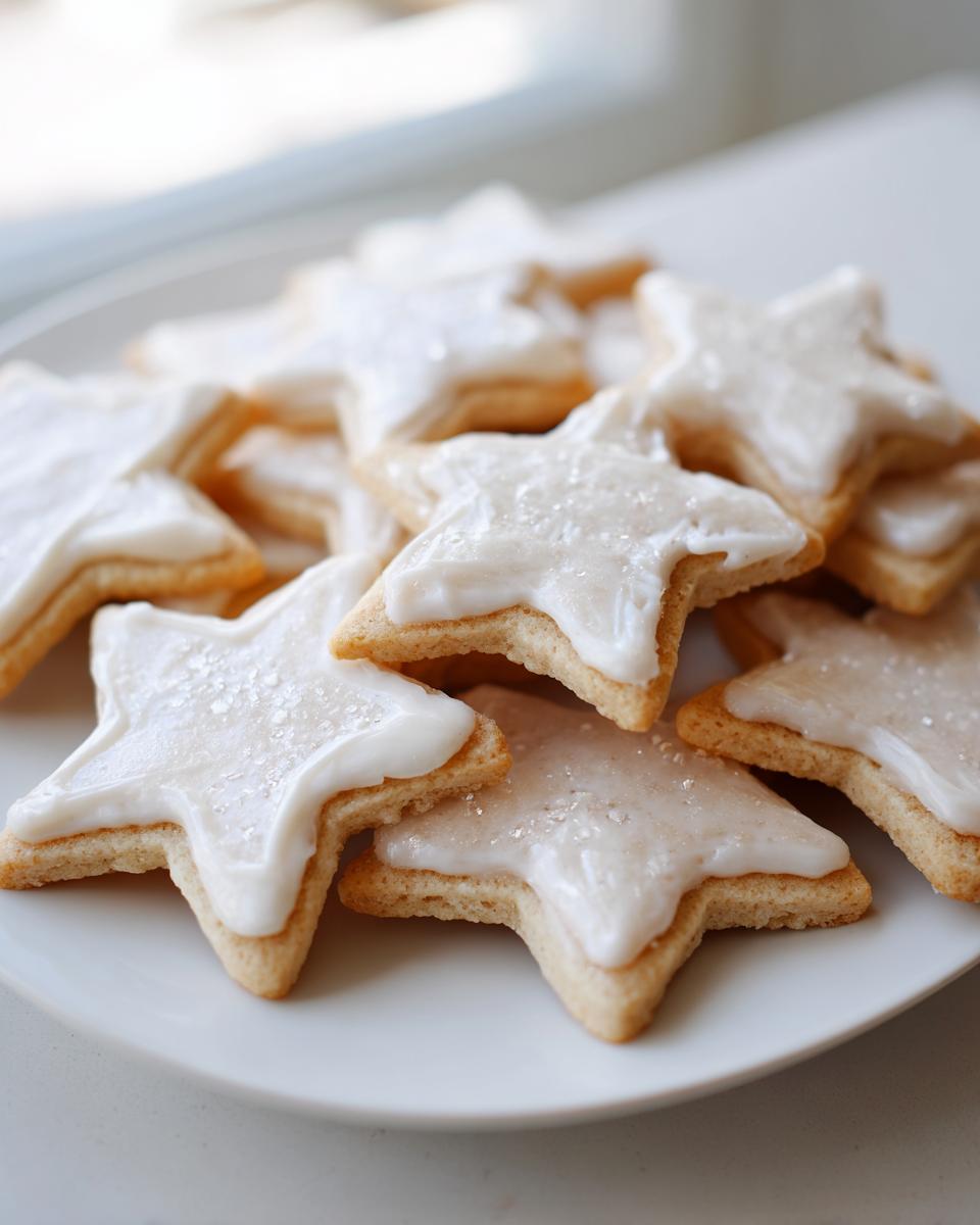 A pile of star-shaped vegan sugar cookies topped with thick white icing and sparkling sugar.