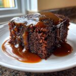 A close-up of a square slice of dark, moist sticky toffee pudding recipe covered in rich toffee sauce.