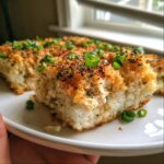 Close-up of a thick slice of creamy sushi bake with a golden, crispy topping and fresh green onions.