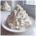A large, beautifully piped mound of fluffy white vanilla buttercream frosting served on a small white plate.