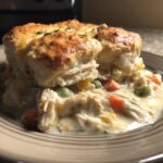 A hearty serving of chicken pot pie with biscuits, featuring shredded chicken and vegetables in a creamy sauce.