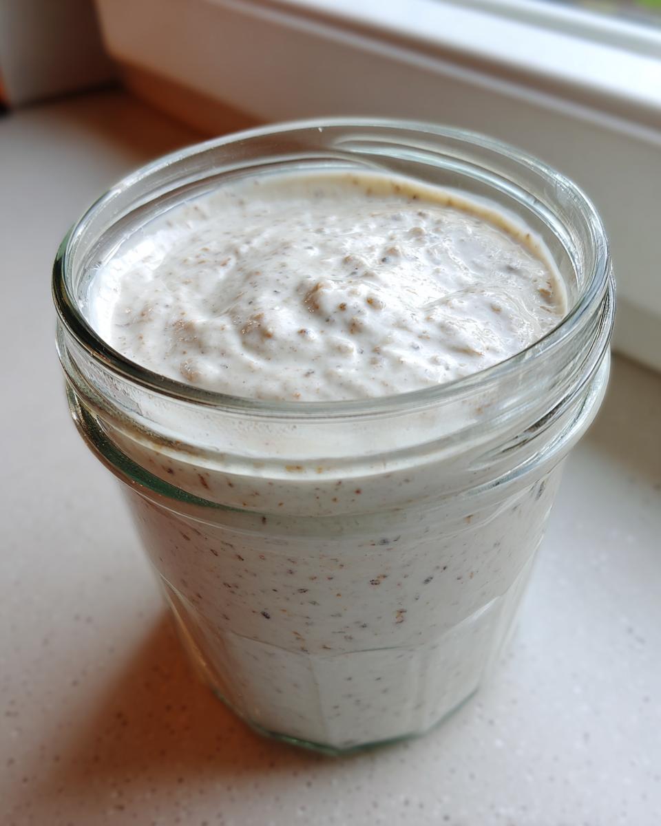 Close-up of creamy, white chia pudding speckled with seeds in a clear glass jar.