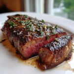 Close-up of a juicy, medium-rare ribeye steak, sliced and topped with garlic and herbs.