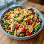 A vibrant bowl of southwest salad featuring shredded chicken, avocado slices, black beans, corn, and orange dressing.