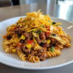 A serving of amazing taco pasta salad featuring rotini pasta, seasoned ground beef, corn, black beans, and topped with cheese and tortilla strips.