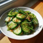 Close-up of a vibrant asian cucumber salad, sliced and dressed with sesame seeds and scallions.