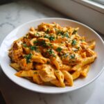 A close-up of creamy cajun chicken pasta featuring penne, chicken pieces, and fresh parsley garnish.