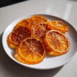 Close-up of glistening candied orange slices sprinkled with sugar crystals on a white plate.