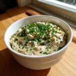 A white bowl filled with creamy caramelized onion dip, generously topped with fresh green chives.