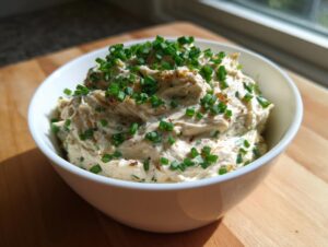 A white bowl filled with creamy caramelized onion dip, generously topped with fresh green chives.