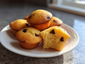 A plate of golden brown chocolate chip pancake muffins, with one muffin broken open showing the fluffy interior.