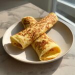 Three golden-brown, rolled cottage cheese wraps displayed on a light ceramic plate in bright sunlight.