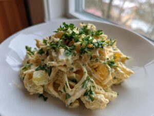 A serving of creamy celery salad mixed with a rich dressing and topped generously with fresh chopped parsley.