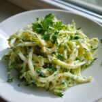 A close-up of creamy celery salad tossed in a light dressing and topped with fresh parsley.