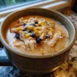 Close-up of creamy chicken taco soup topped with shredded chicken, black beans, corn, and melted cheese.