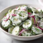 Close-up of sliced cucumbers coated in a creamy dressing with fresh dill and red onion, showcasing the creamy cucumber salad.