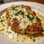 Close-up of a pan-seared chicken breast smothered in rich, creamy garlic sauce and topped with fresh parsley.