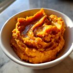 Close-up of creamy mashed sweet potatoes topped with melted butter in a white bowl.