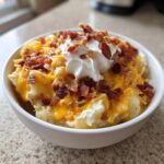 A bowl of thick, creamy potato soup topped generously with shredded cheddar cheese, bacon bits, and sour cream.