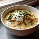 A close-up of a bowl of creamy white chicken chili recipe, topped with sour cream and fresh cilantro.
