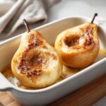 Close-up of two halved baked pears, caramelized with cinnamon sugar, sitting in a white baking dish.