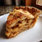 Close-up of a thick slice of homemade apple pie showing flaky crust and chunky cinnamon apple filling.