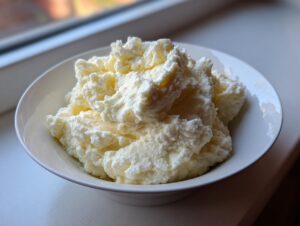 A white bowl filled with light, fluffy, and slightly textured mashed potatoes recipe, set near a window.