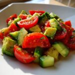 Close-up of a fresh avocado salad featuring bright red tomato wedges and green cucumber chunks.