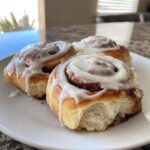 Three gooey cinnamon rolls generously topped with white icing, resting on a white plate.