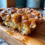A close-up, mouthwatering shot of a slice of snickerdoodle cobbler covered in thick caramel sauce and coarse sugar.