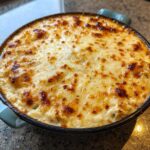 Close-up of a hot, baked crab dip recipe topped with bubbly, golden brown melted cheese.