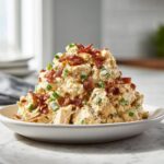 A mound of creamy jalapeno popper chicken salad topped with crispy bacon bits and green onions.