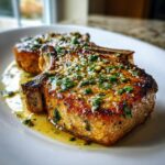 Two thick, juicy pork chops seared golden brown and topped with garlic butter sauce and fresh parsley.