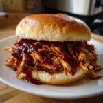 Close-up of a delicious pulled chicken sandwich smothered in BBQ sauce on a soft bun.