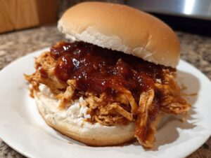Close-up of a juicy pulled chicken sandwich smothered in BBQ sauce on a white bun.