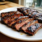 Close-up of perfectly grilled and sliced skirt steak showing a medium-rare center on a white plate.