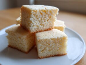 Close-up of light, buttery squares, possibly shortbread cookies, stacked on a white plate.